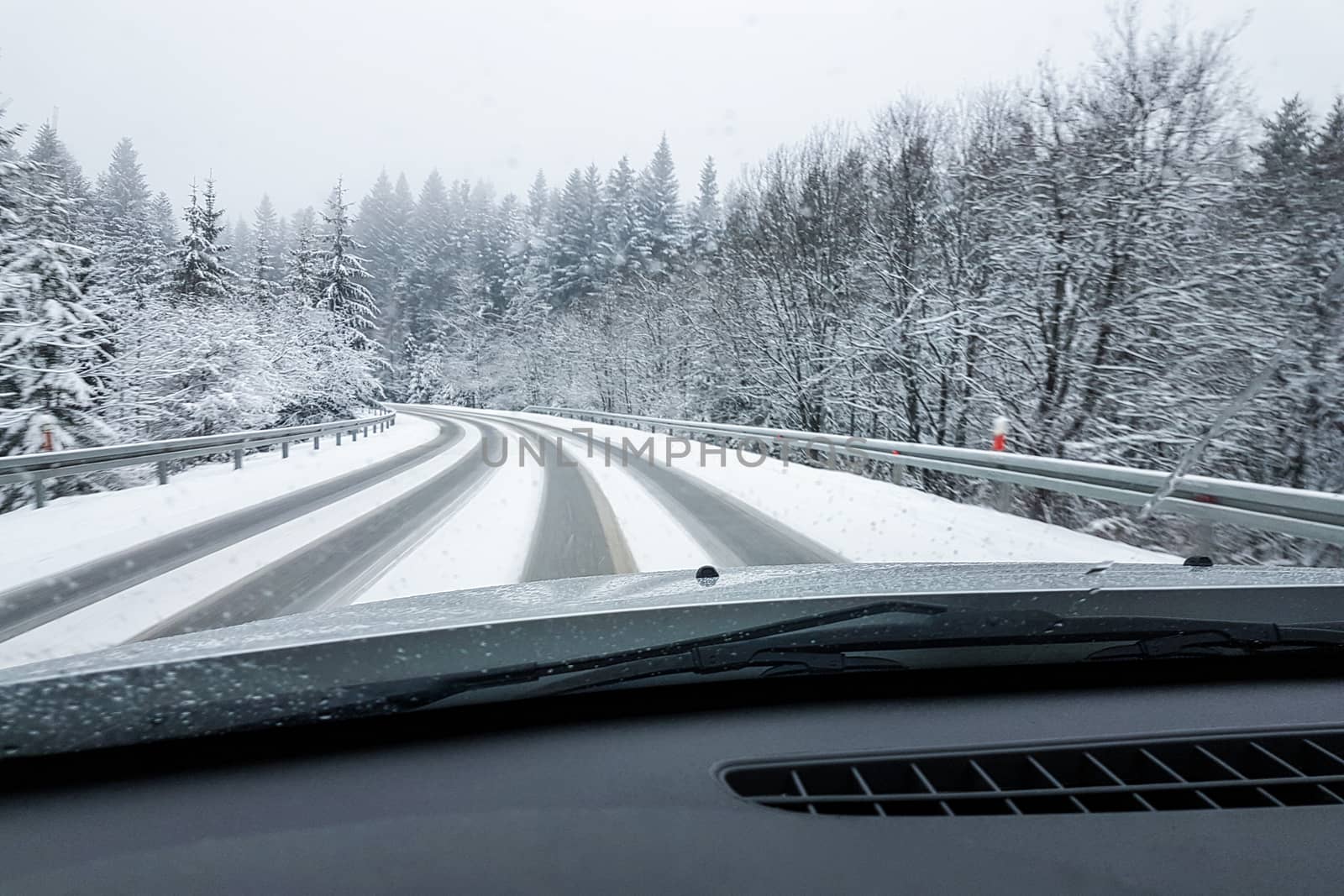 Driving a car in bad weather - a front window view of a snowy road during  in winter on a foggy day.