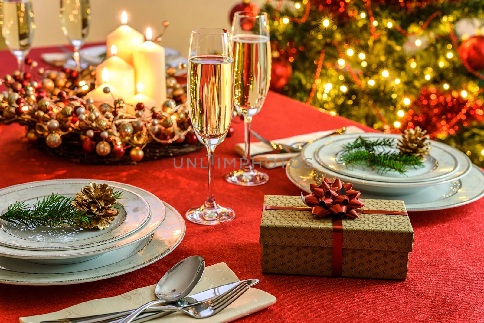 Beautifully decorated Christmas table - gift, glasses of champagne and tableware with Christmas decoration on a red tablecloth.