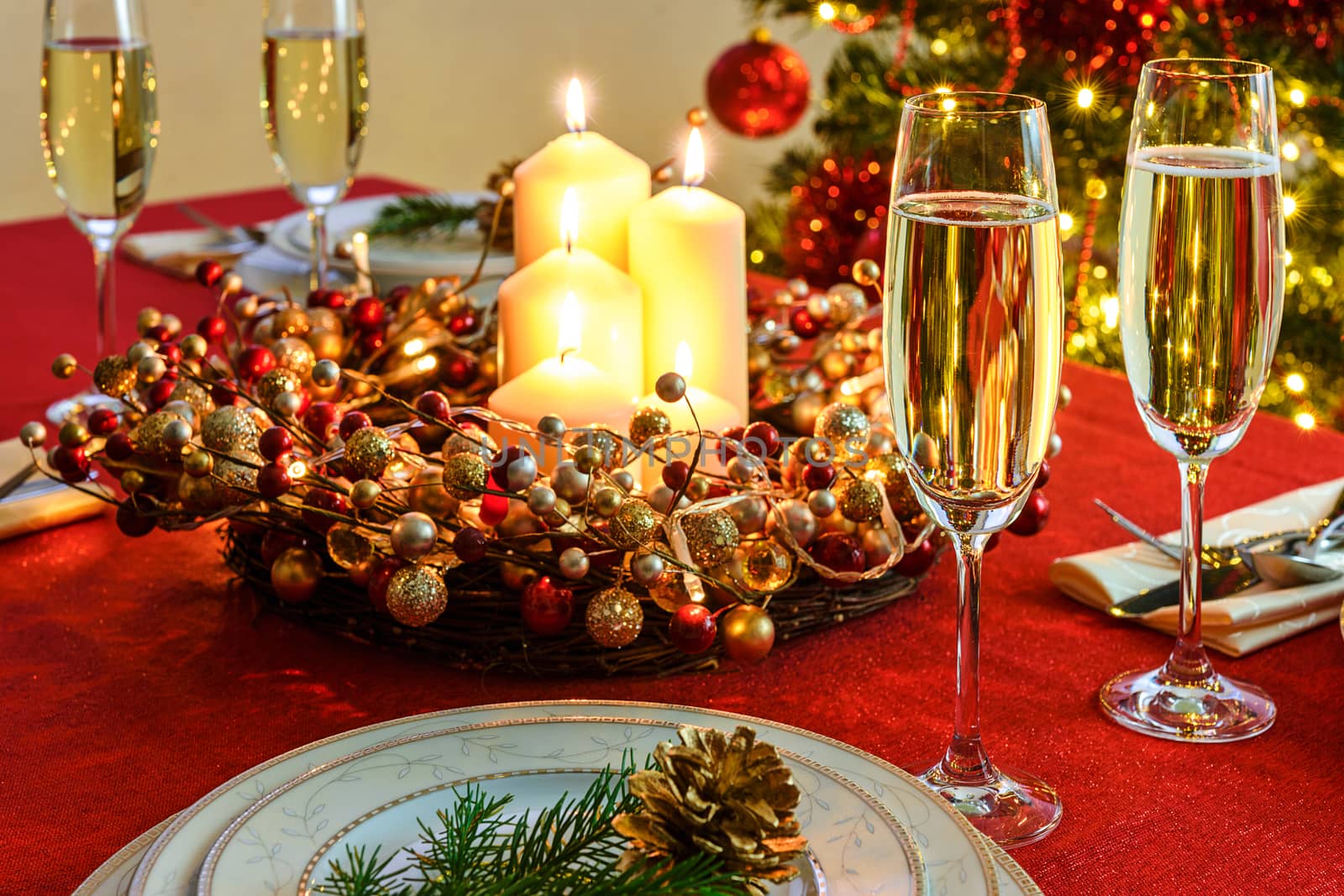 Beautifully decorated Christmas table - glasses of champagne and tableware with Christmas decoration on a red tablecloth.