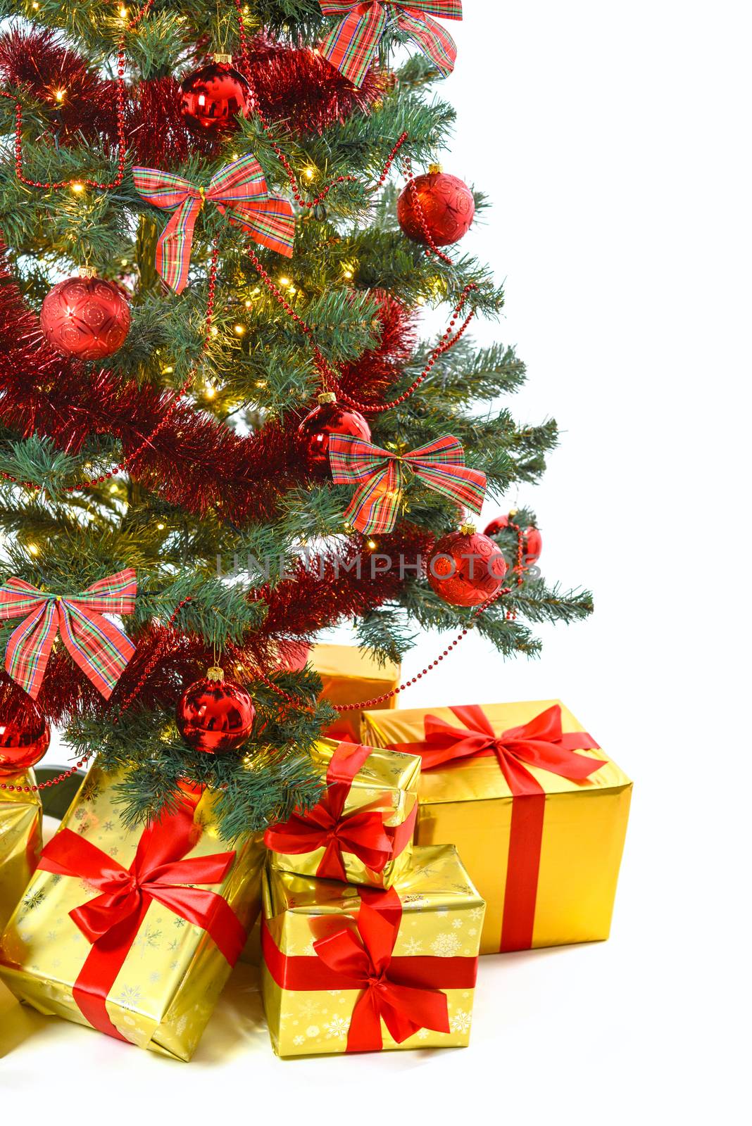 Luxury golden colored gifts with red ribbon under a beautiful christmas tree with red balls, bows and lights isolated on white background in close-up