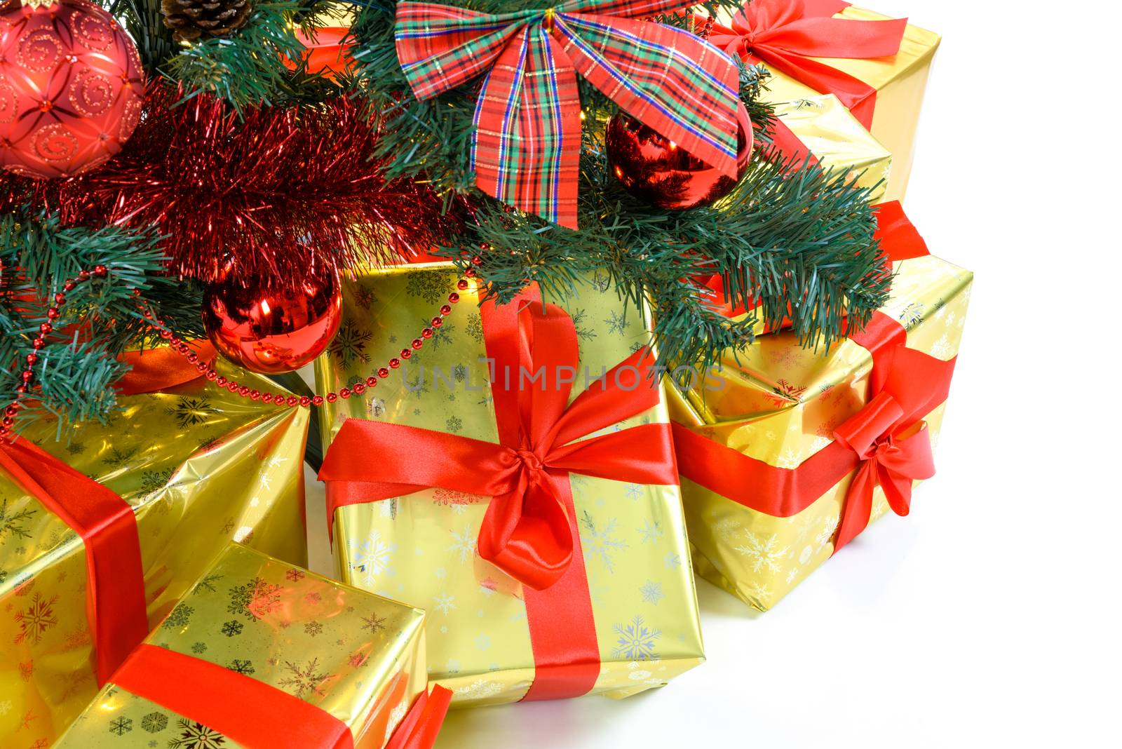 Luxury golden colored gifts with red ribbon under a beautiful christmas tree with red balls, bows and lights isolated on white background in close-up