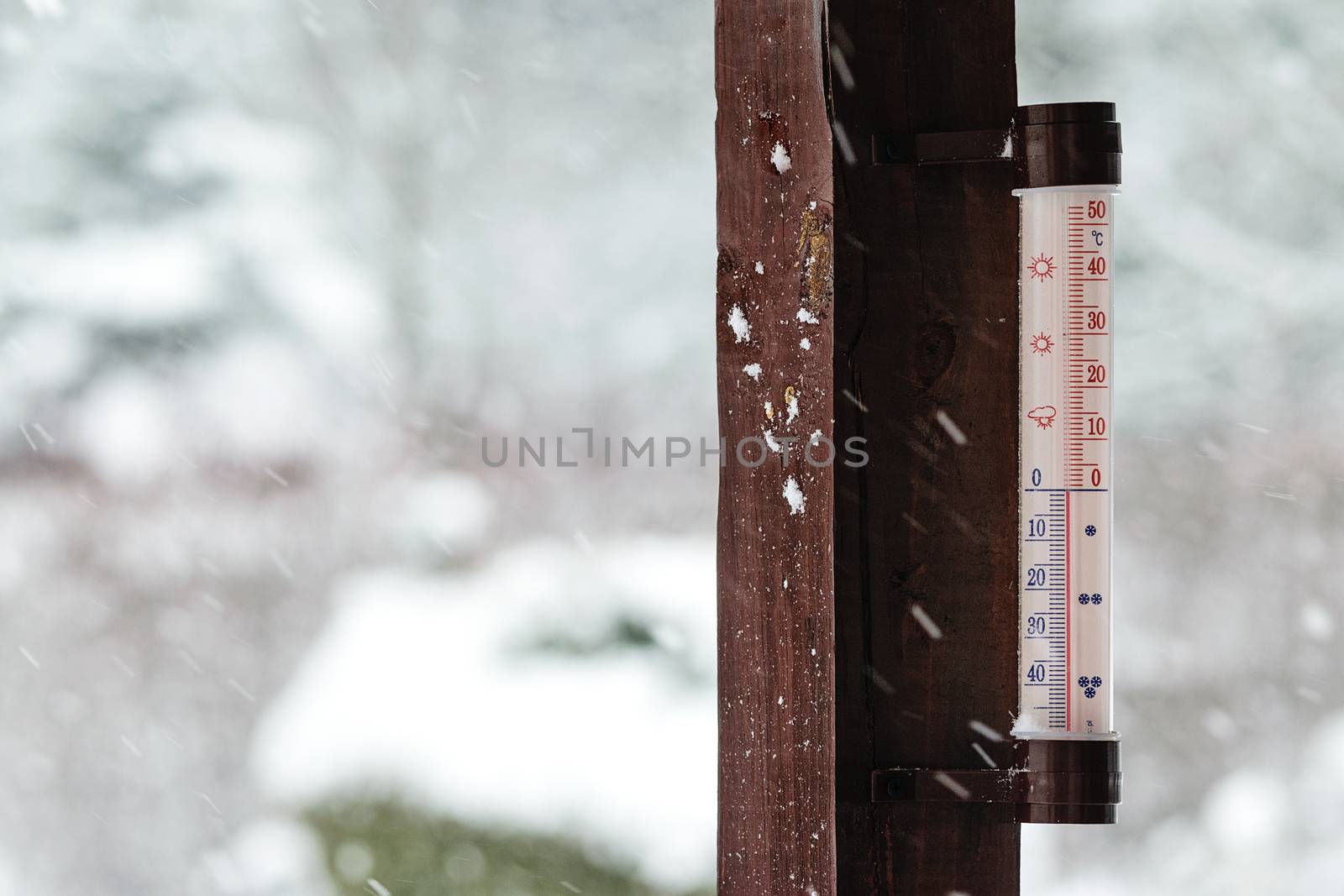 Concept image of winter coming - thermometer outside the house indicates below zero and it is snowing heavily.