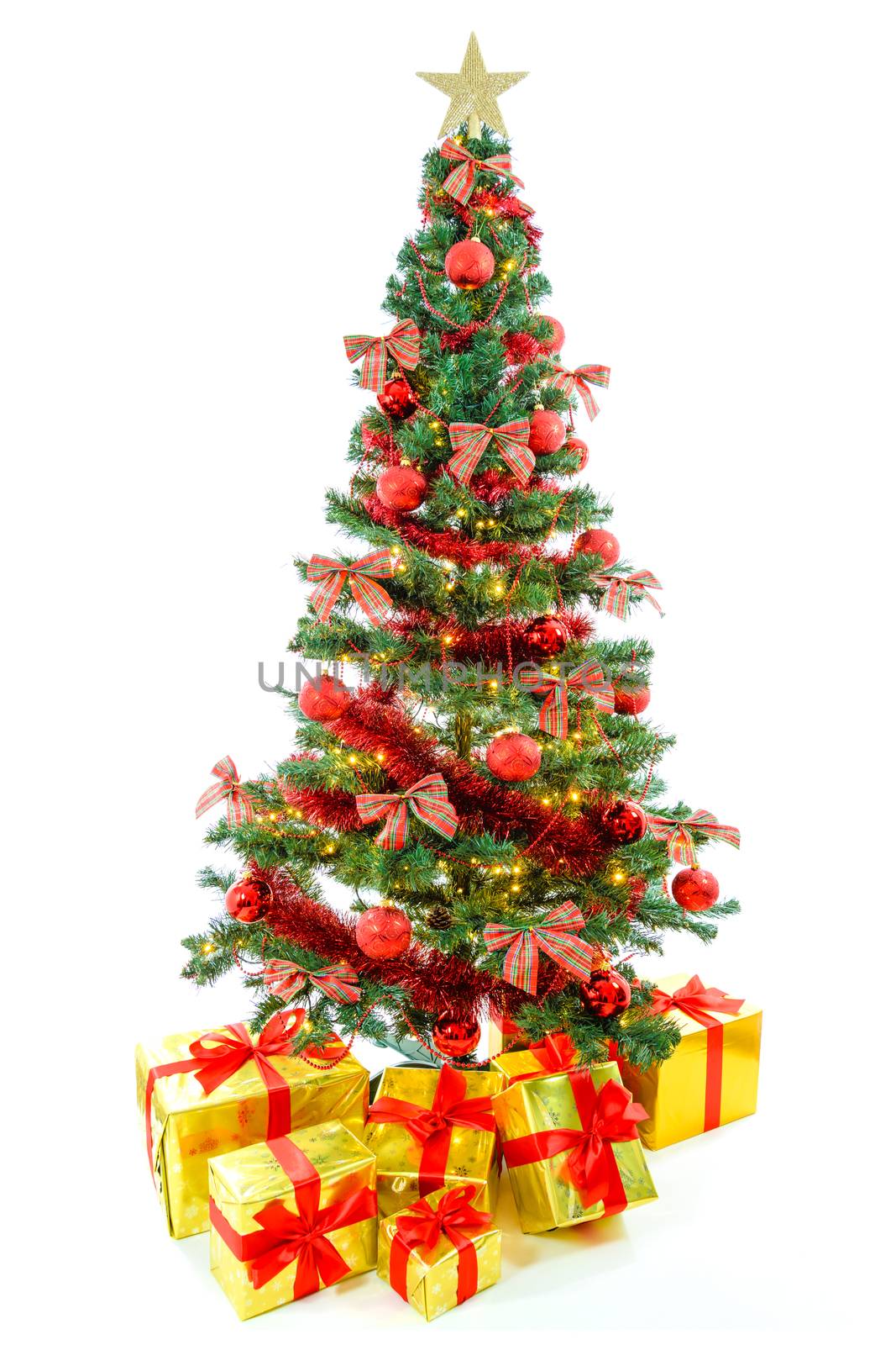 Luxury golden colored gifts with red ribbon under a beautiful, large christmas tree with red balls, bows and lights isolated on white background.
