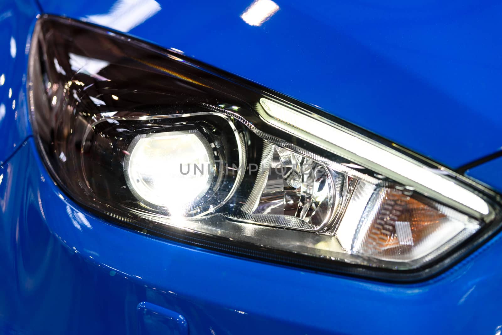 Glossy headlamp in a modern blue car in close-up. 