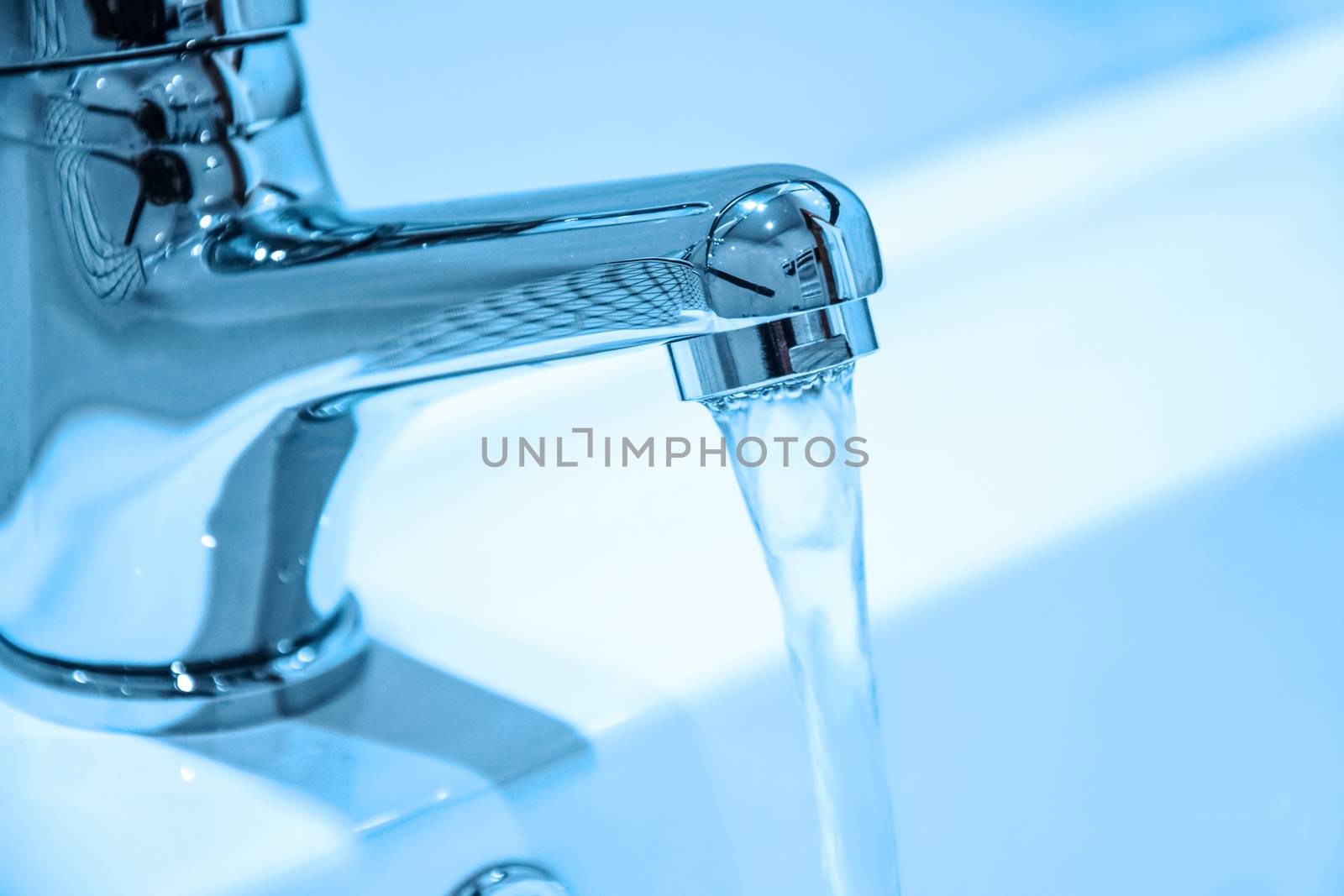 Water running from an open faucet in close-up (blue filter effect).