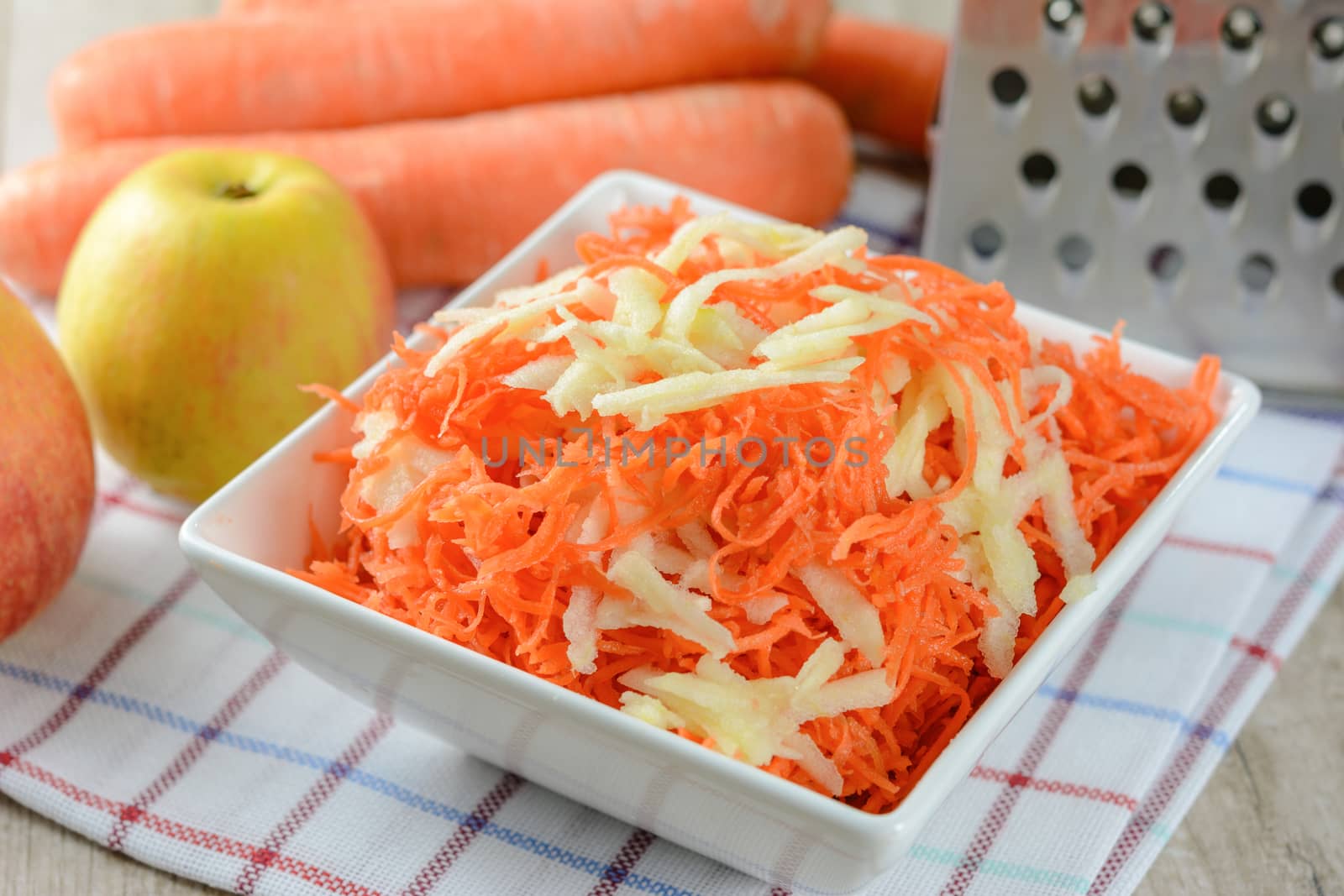 Concept of preparing a healthy salad - grated carrot with apple in a white platter on a background of graters, carrots and apples