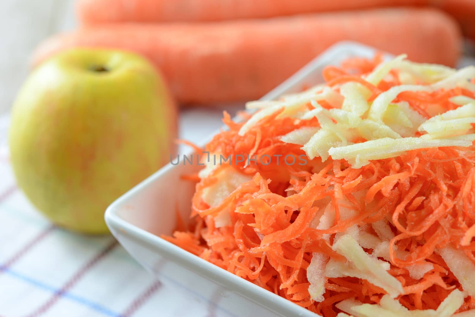 Healthy salad concept - grated carrot with apple in a white platter in close-up