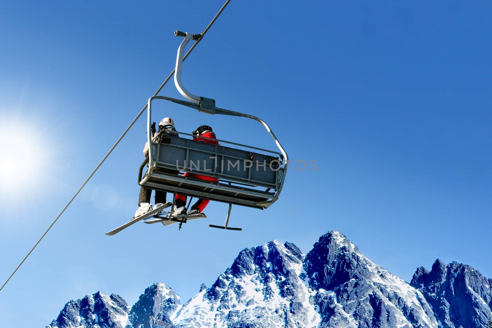 Skiers on a ski lift in high mountains on the background of a clear blue sky with copy space.