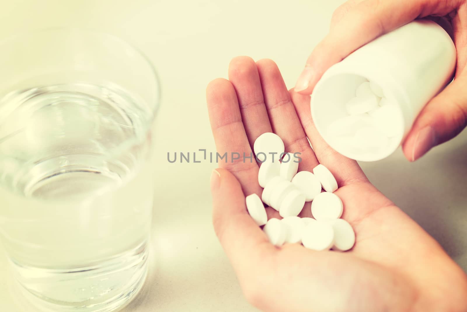 Concept image of drugs addictions - hand of young woman with many pills and water in close-up (vintage effect).