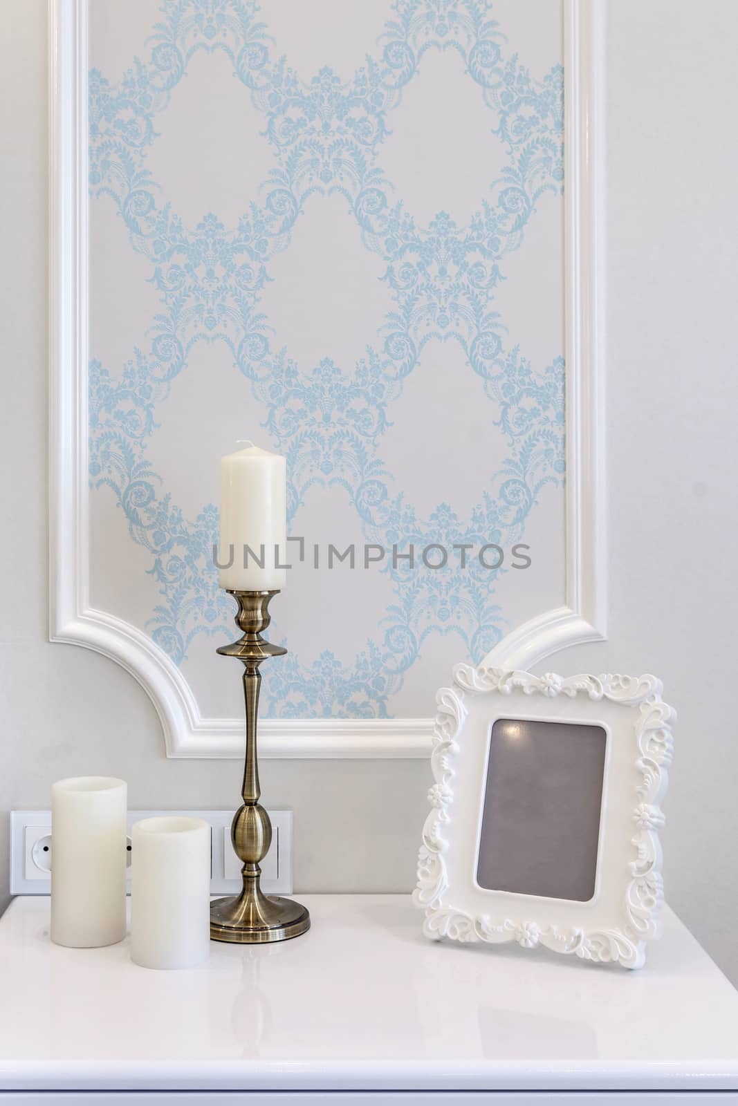 Fragment of a room with a white table. Vintage photo frame and candlestick on a white table.