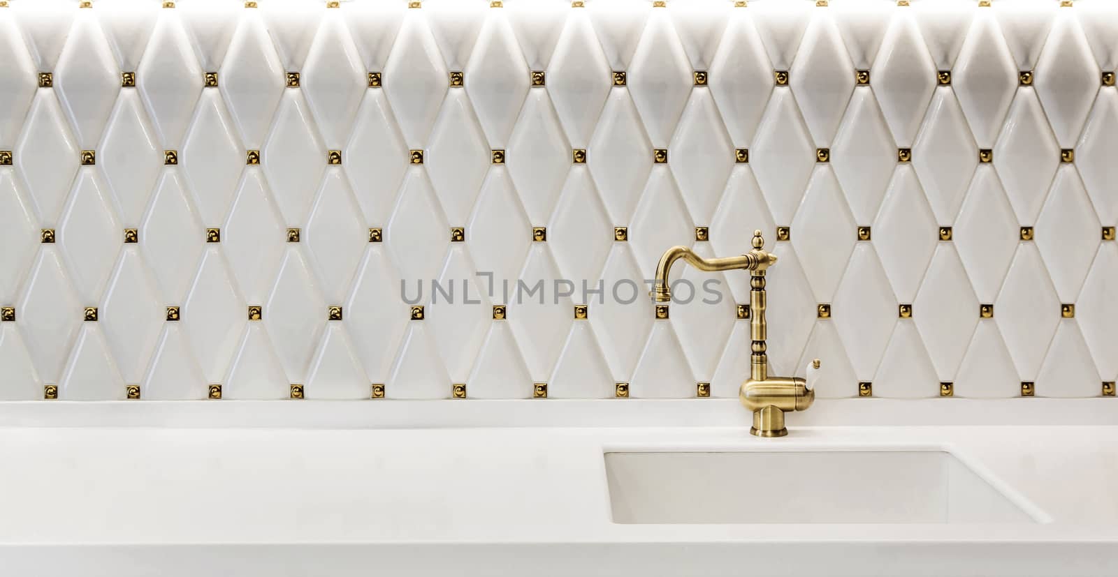 Fragment of a modern kitchen. Sink with faucet made of bronze on a white glossy kitchen worktop.