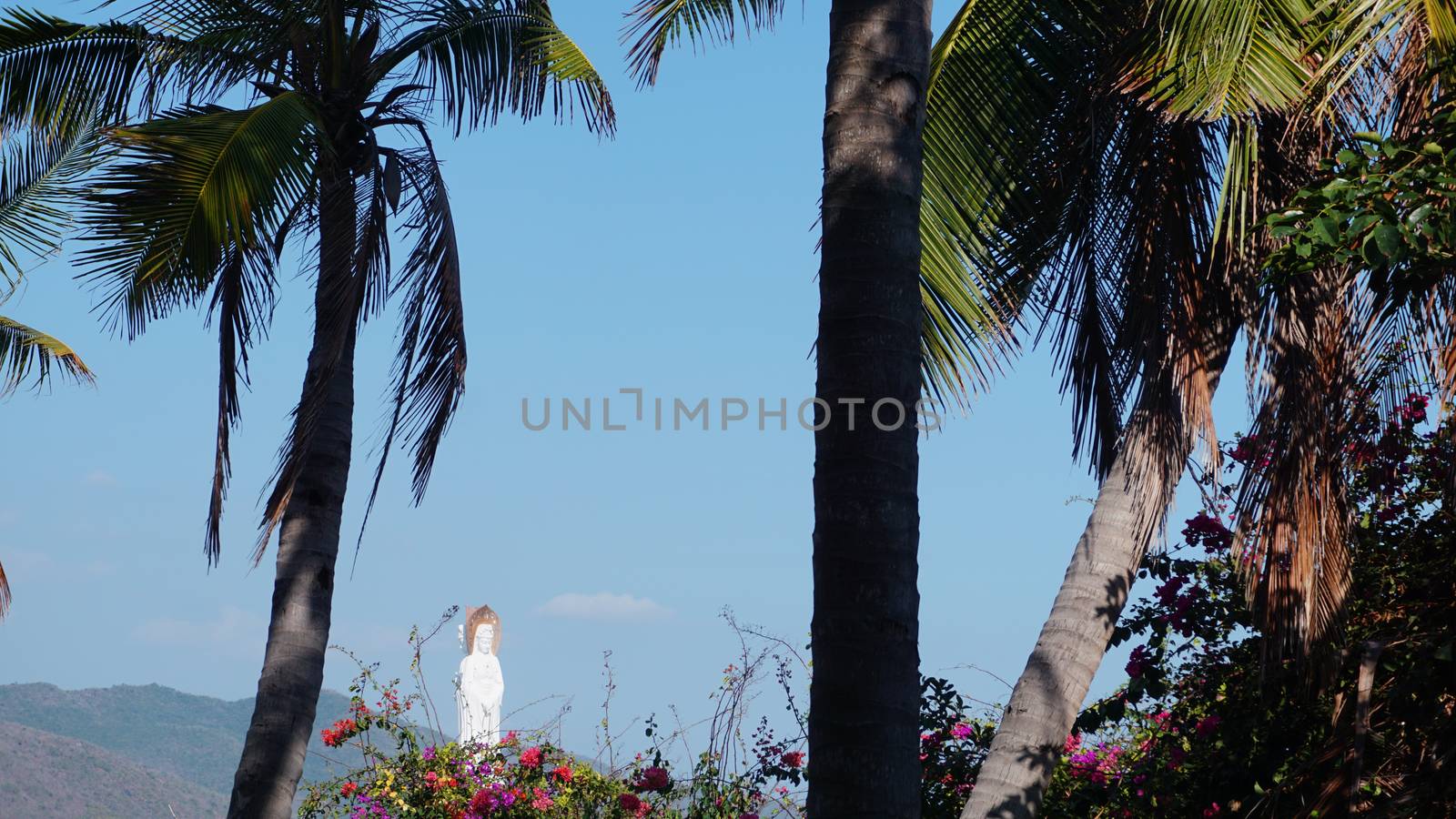 Sanya, Hainan, China - Landscape with tropical palm trees and Goddess of Mercy located in the sea against blue sky in Nanshan Buddhist Cultural Centre
