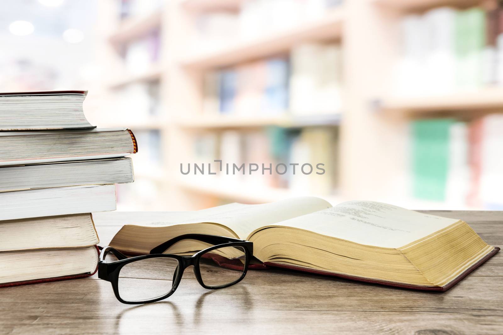 Concept image of education and learning - stocks of books next to open book and eyeglasses on a desk in the library.