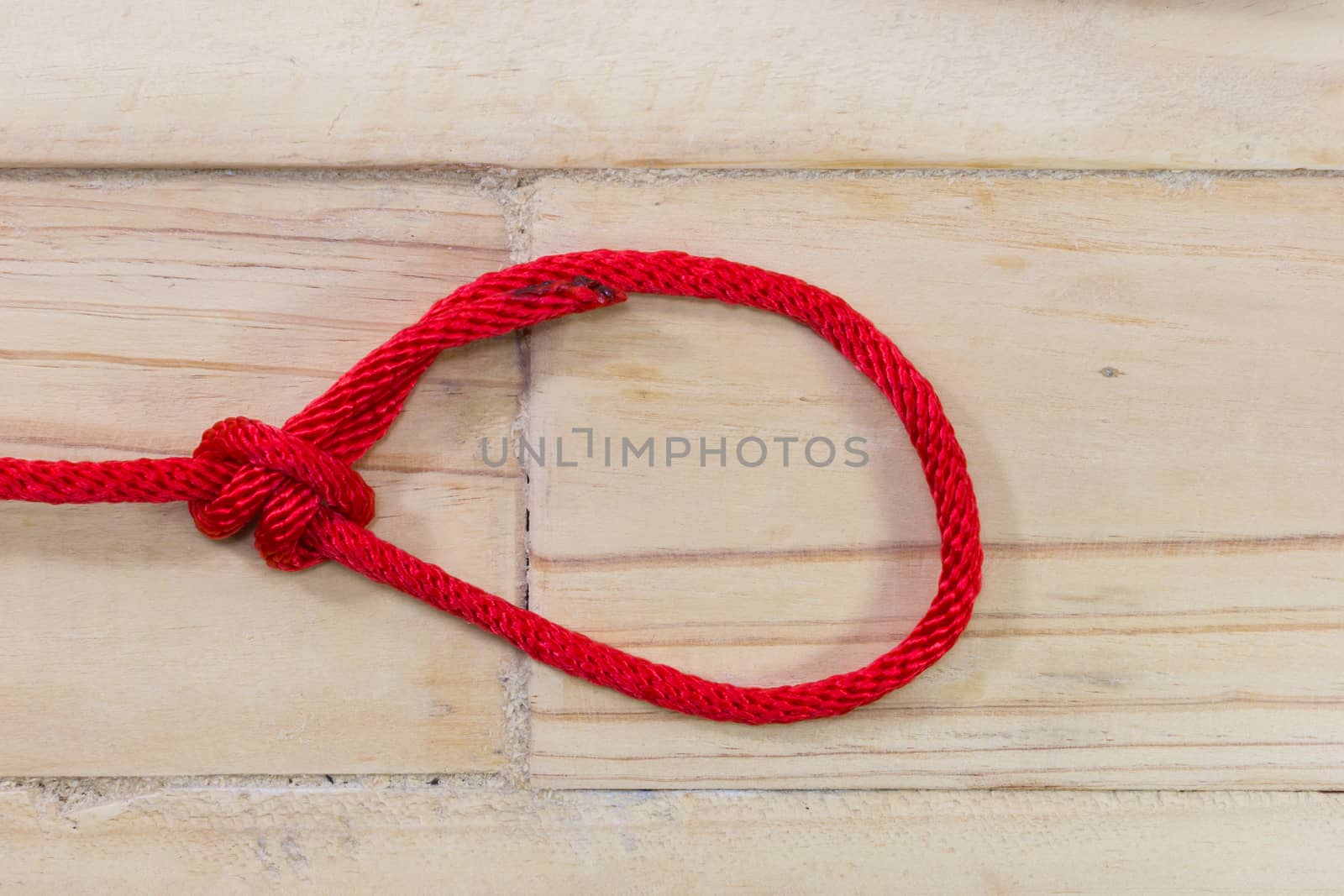 bowline knot made from red synthetic rope, tightening on wooden background.