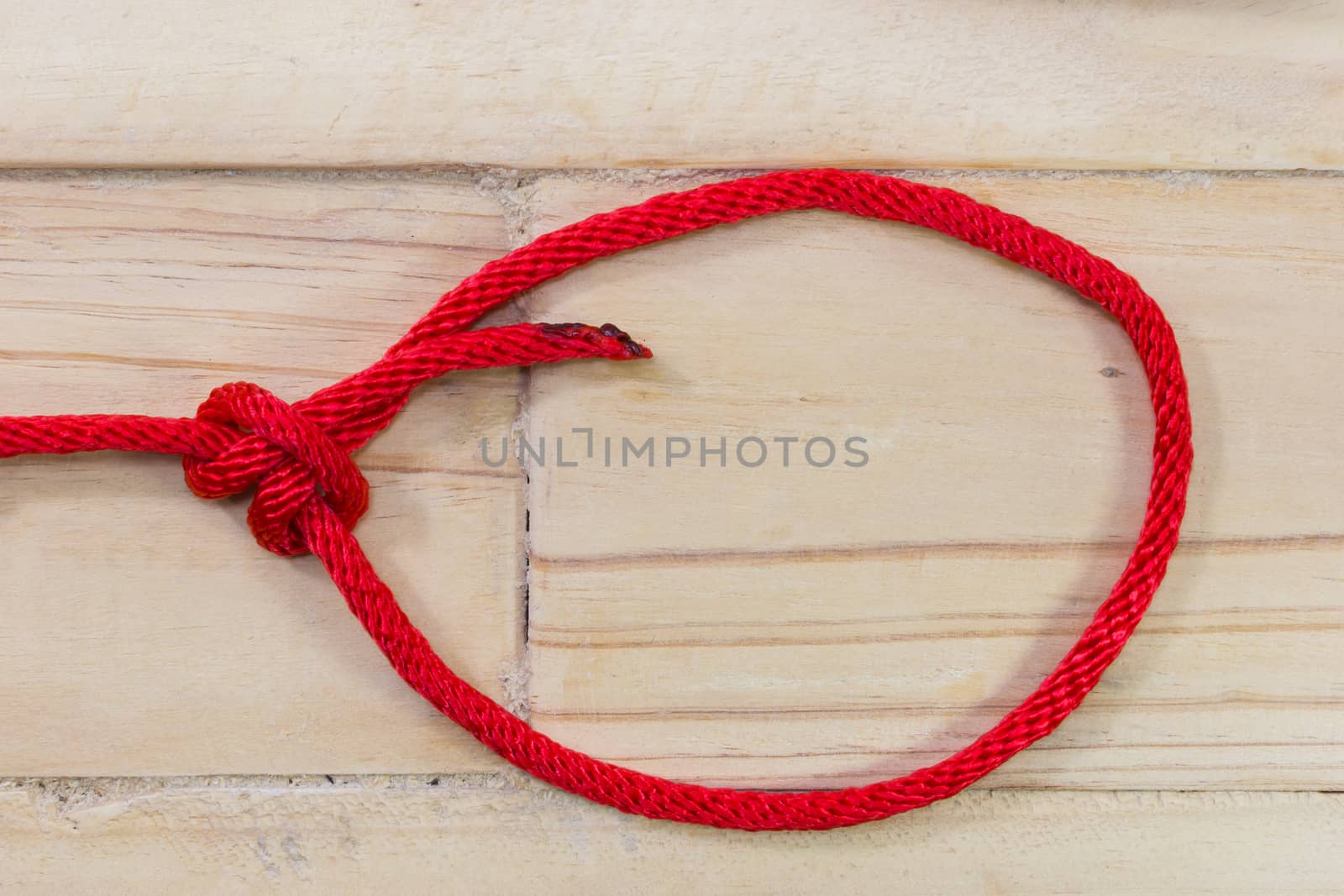 bowline knot made from red synthetic rope, tightening on wooden background.