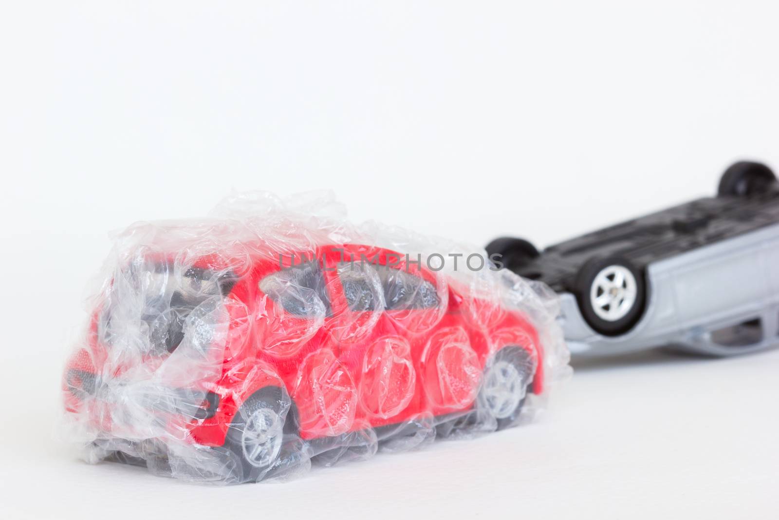 horizontal photo of two cars toy in accident scene. The safe red one is protected with air bubble on blank background.