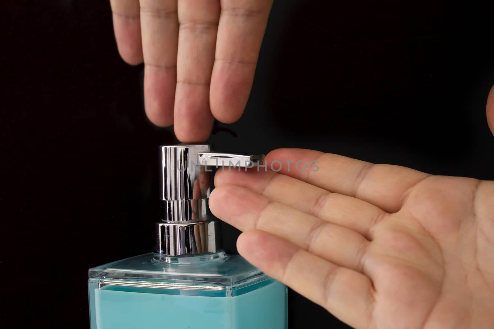 Close up of a person getting soap from a soap dispenser on a black background