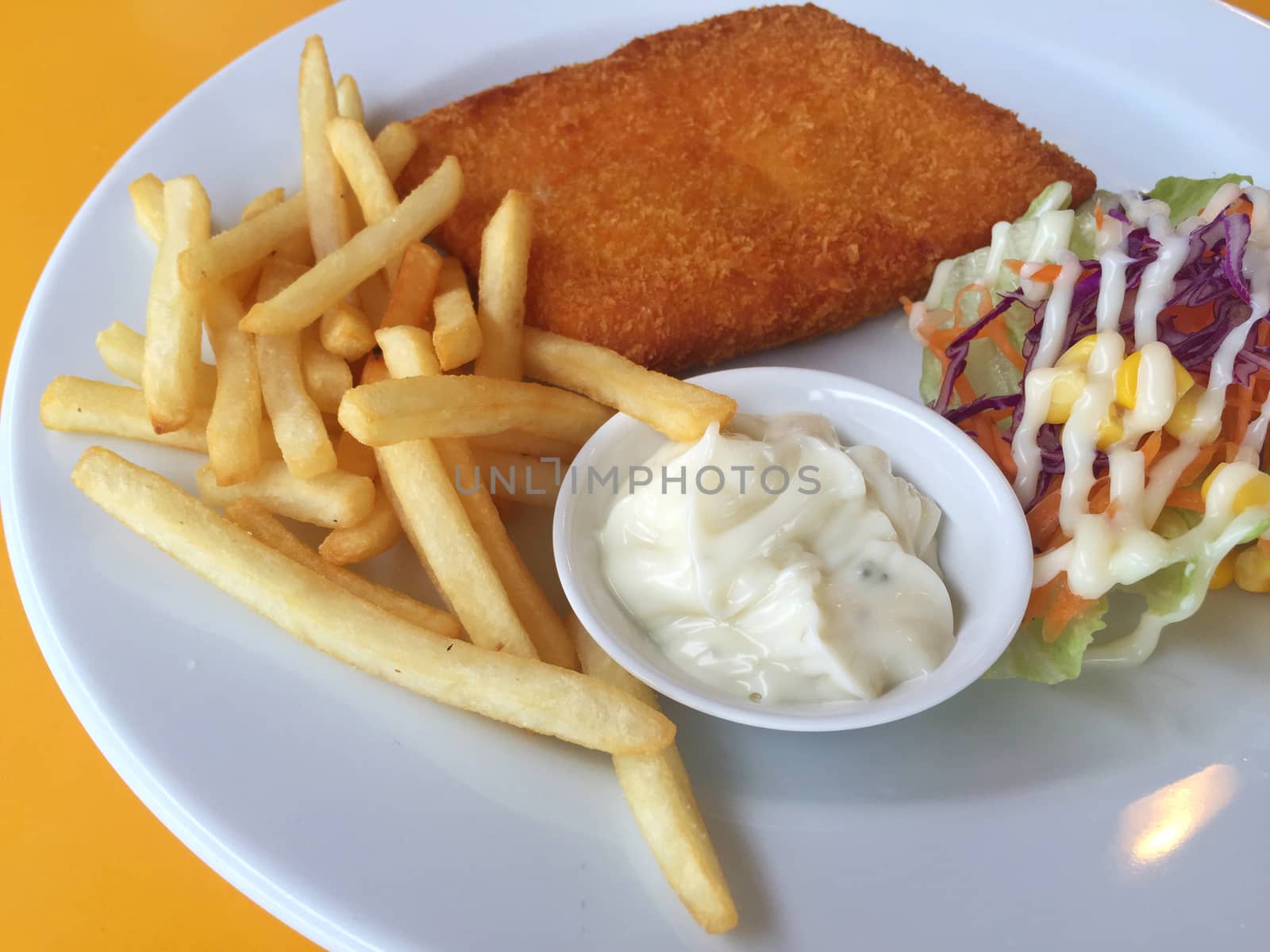 closeup fried fish, chips and salad on a white dish on yellow table background. Horizontal photo