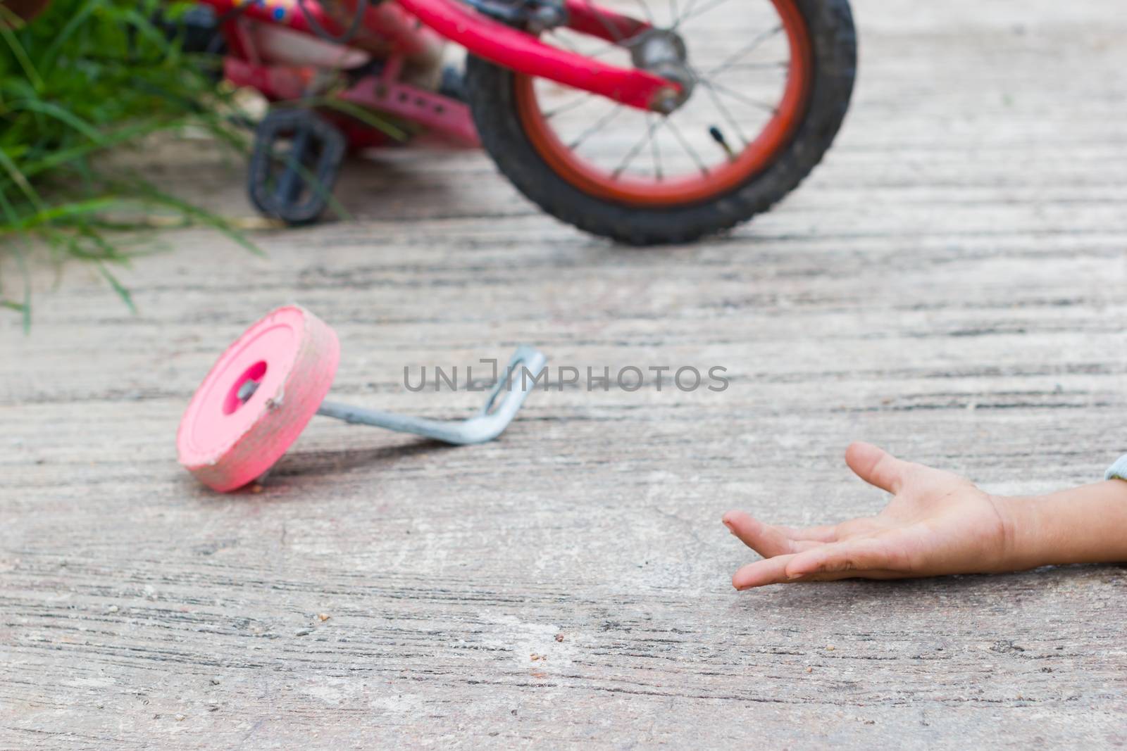 horizontal photo of closeup bicycle for children accident on the city street with hand of a child on the ground