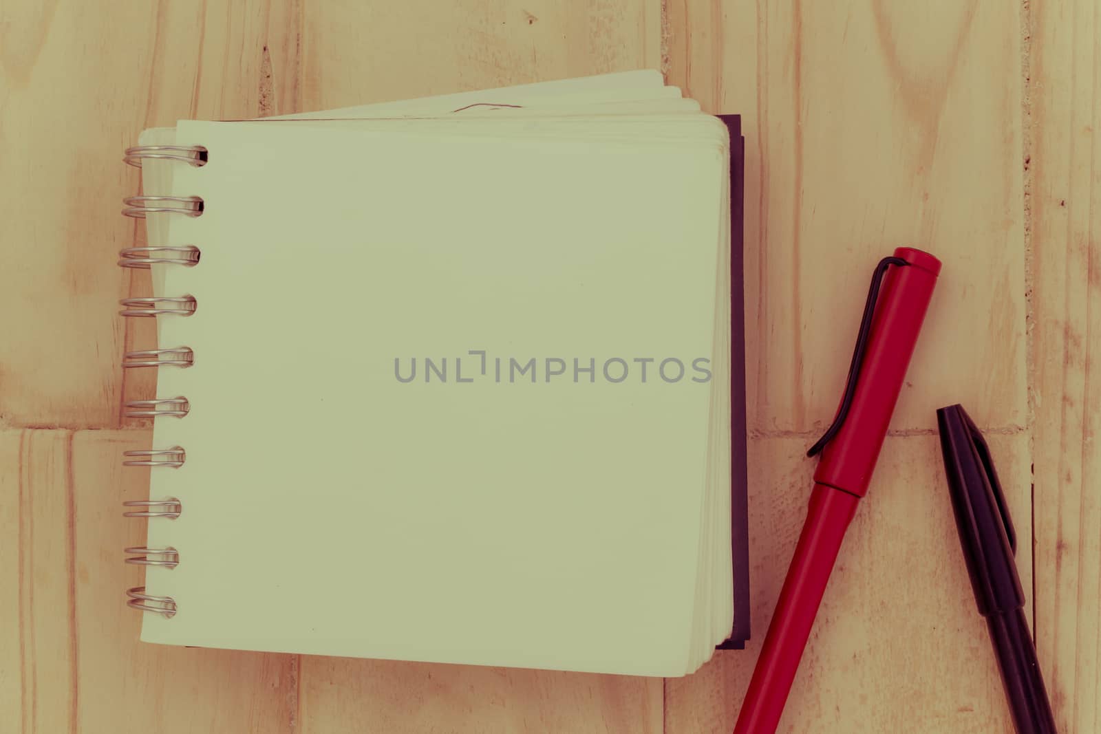 closeup blank notebook on a brown wooden table, with red and black pen, vintage retro style