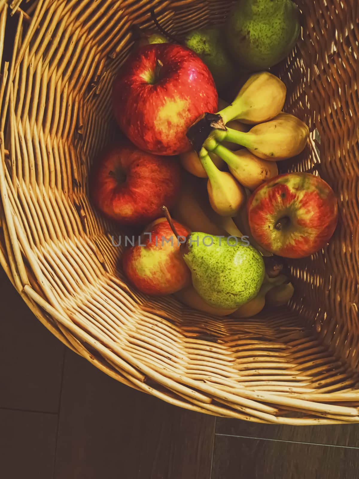 Organic apples, pears and bananas on rustic in a wicker basket by Anneleven