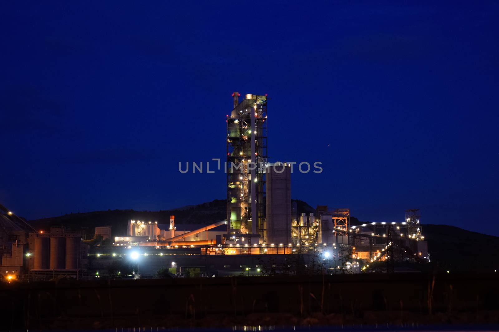 The building of a cement plant at night, the lights of a lamp lighting a factory. Industrial facility.