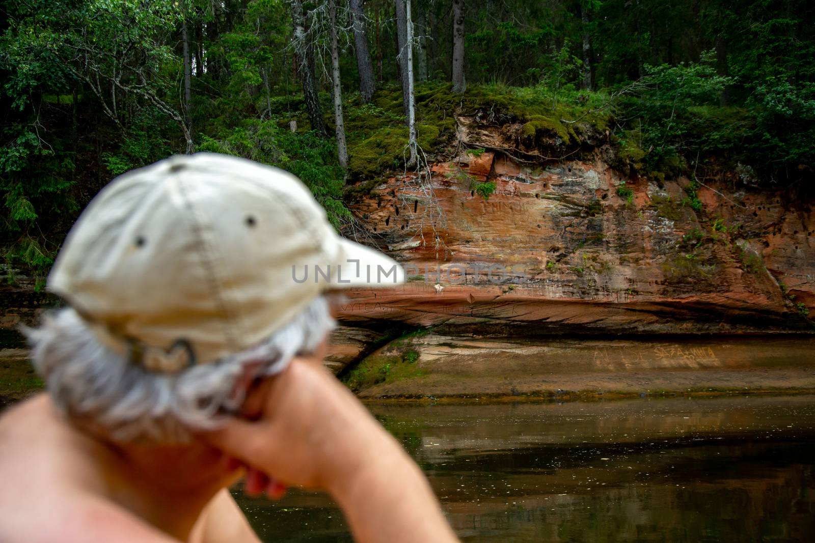 Man at the rock. Portrait of man at the rock,  on coast of the river. The man looks at the cliff. Rock on the Gauja river. Cliff is steep rock face, especially at the edge of the river or the sea. Man is out of focus.

