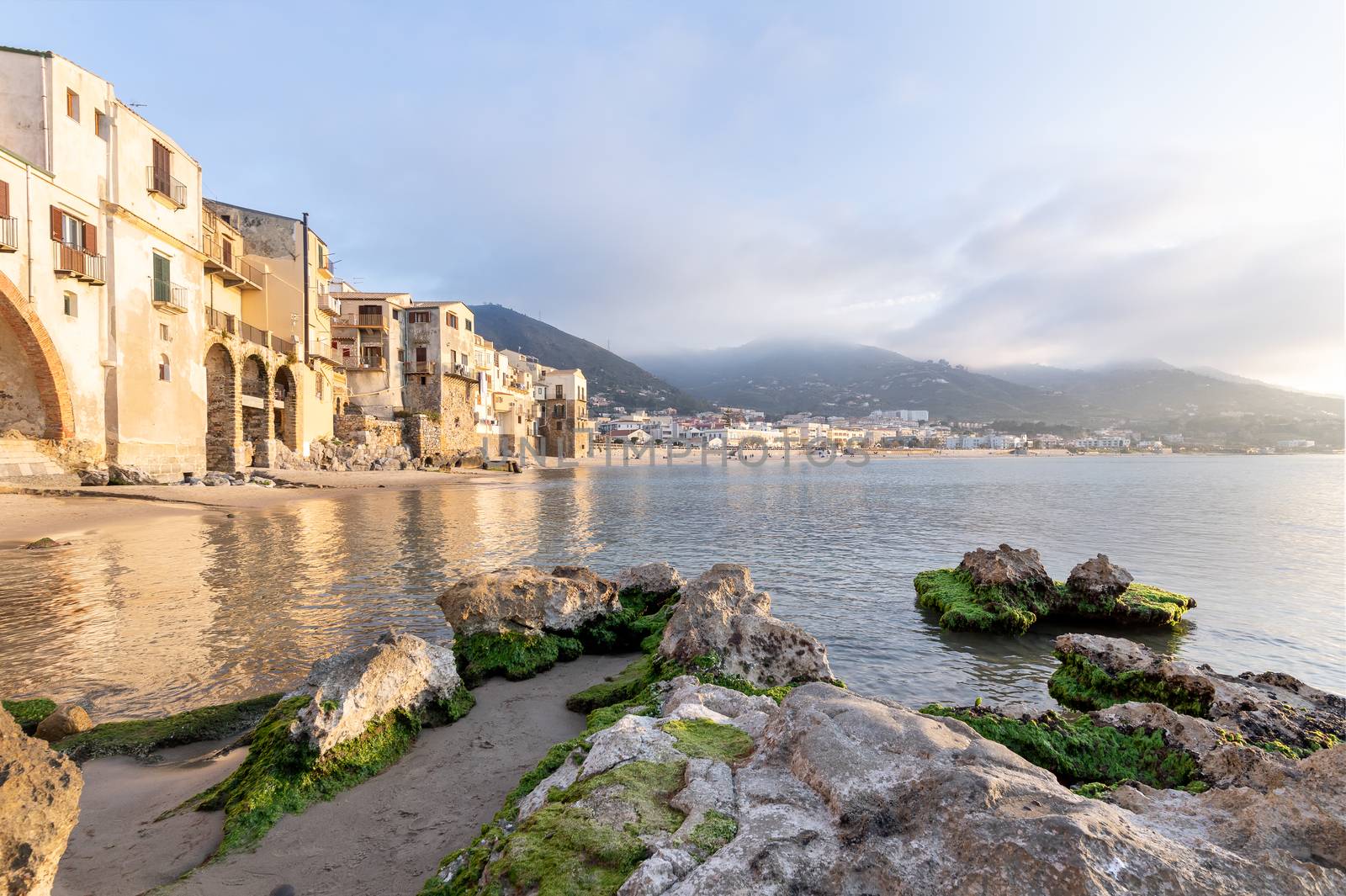 Idyllic view of houses and long sandy beach seen from the old harbour on a sunny day in Cefalu, Sicily, Southern Italy.