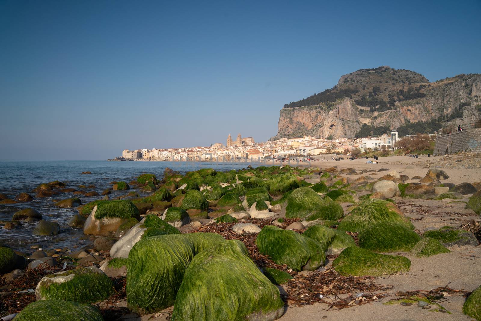 Idyllic view of Cefalu from the long sandy beach. Cathedral and Rocca di Cefalu rocky mountain on a sunny day in Cefalu, Sicily, Southern Italy.