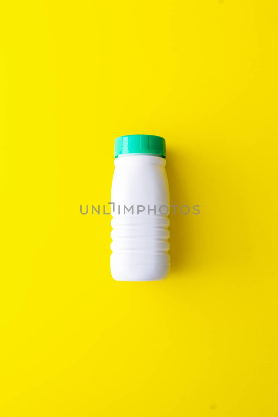 White plastic bottle with a green cap on a yellow background located in the center. Recycling plastic to the yellow container