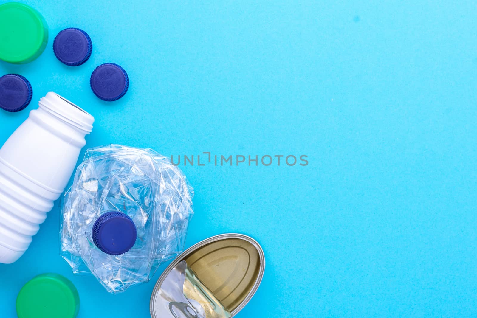 Recycling garbage. White plastic bottle, green cap, blue caps, can of sardines grouped on the left side diagonal on a blue background.