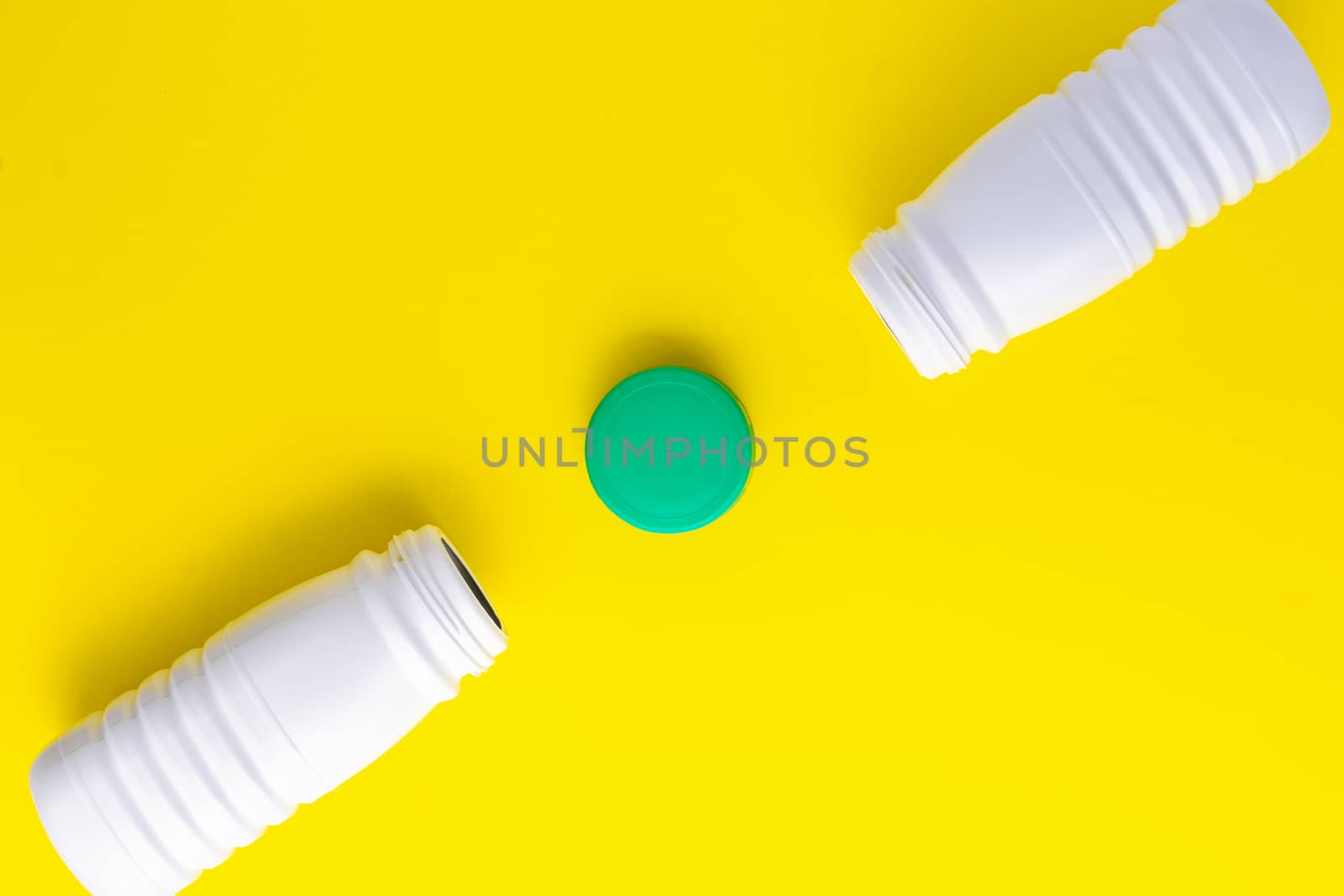 White plastic bottles placed diagonally with a green cap in the middle on a yellow background. Recycling plastic to the yellow container