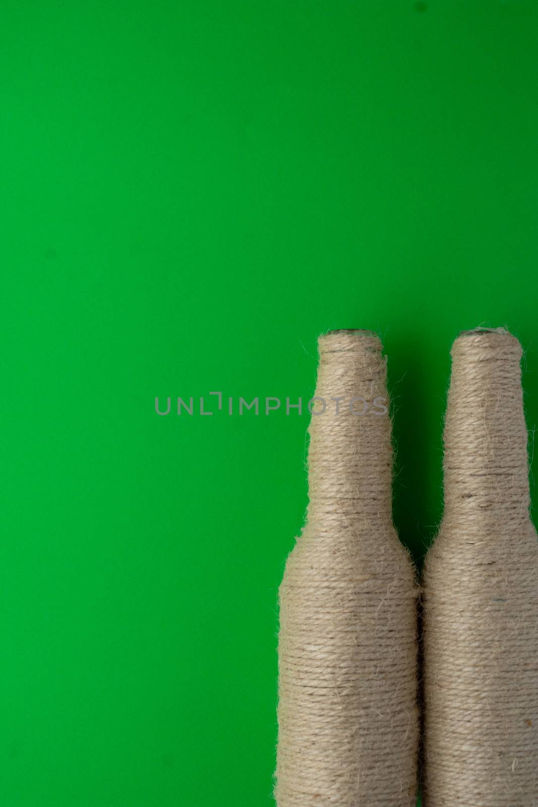 Two glass bottles of beer reused with hemp thread with a green background on the right. Recycling and reusable concept