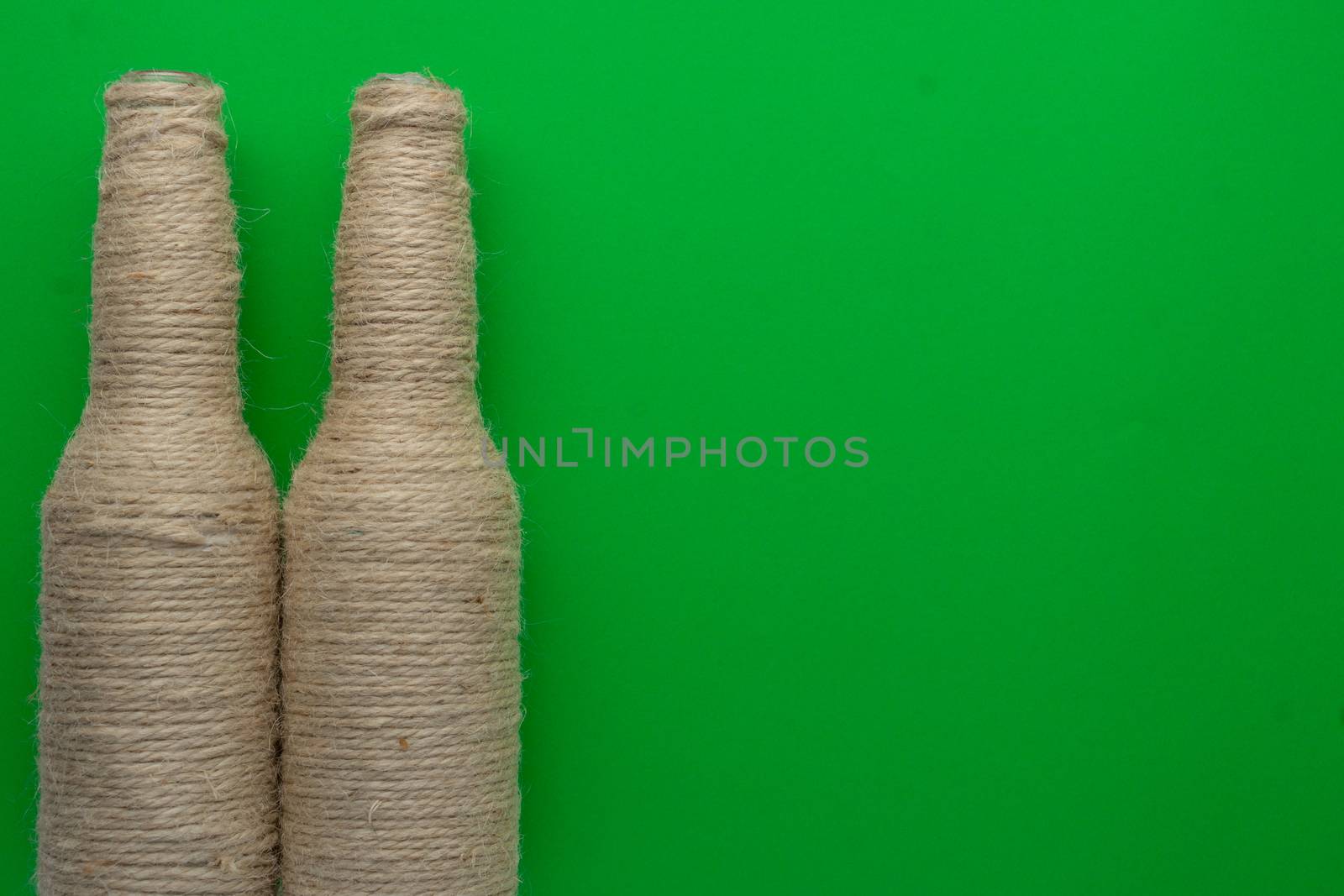 Two glass bottles of beer reused with hemp yarn on the left with a green background. Recycling and reusable concept