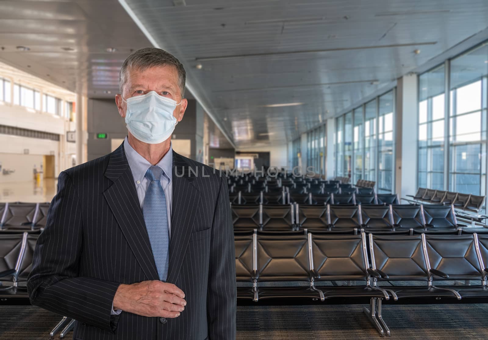 Senior adult executive wearing suit and face mask to travel through airport due to coronavirus