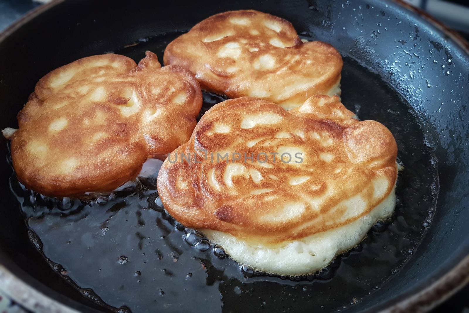 Concept of home cooking for breakfast or lunch - pancakes with apple fried in hot oil in a pan in close-up