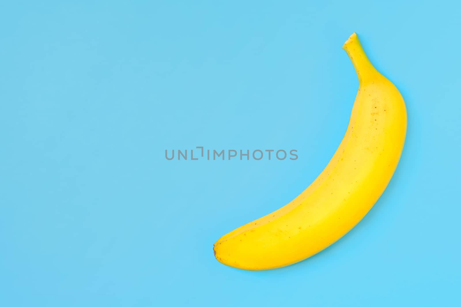 Funny concept image - single banana isolated on a trendy turquoise background in top view with copy space.