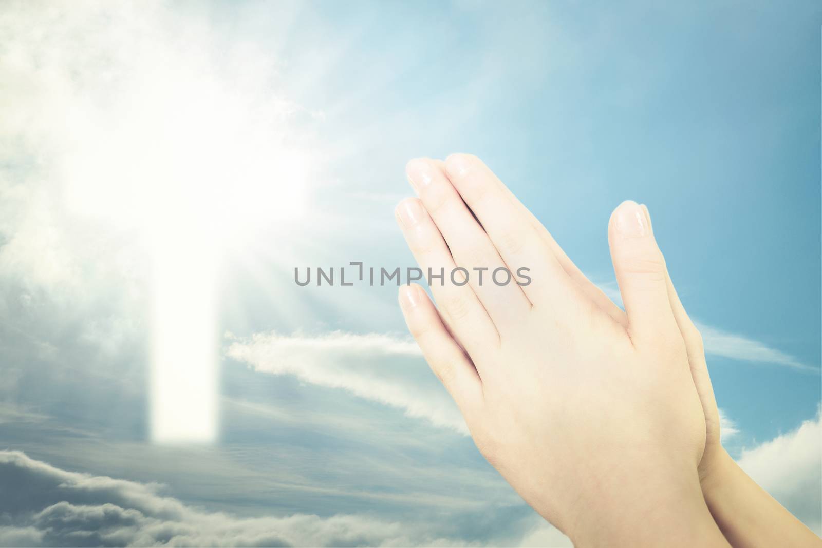 Concept of Christian prayer - folded hands for prayer against a blue sky and a shining cross sign (mixed)