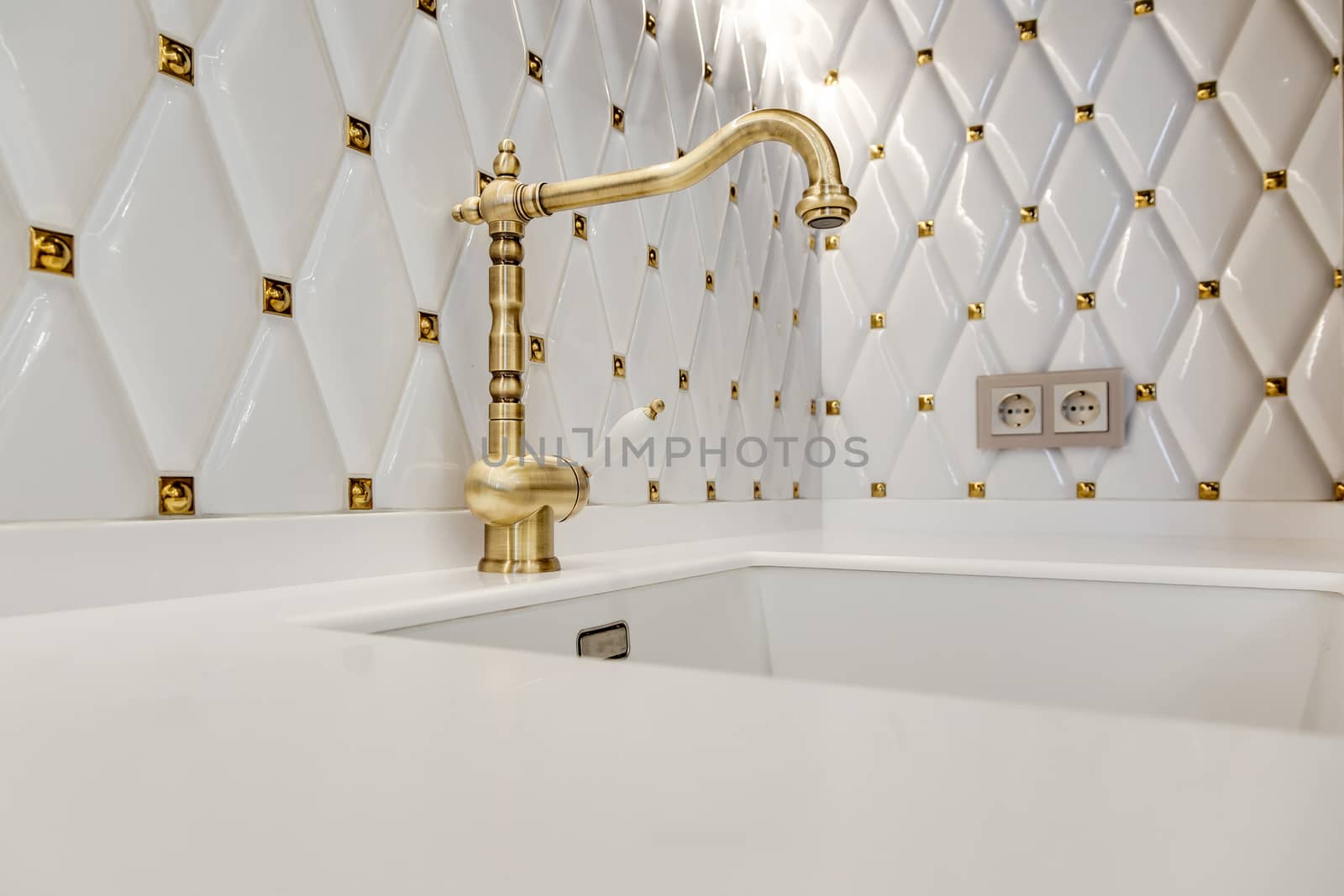 Fragment of a modern kitchen. Sink with faucet made of bronze on a white glossy kitchen worktop.