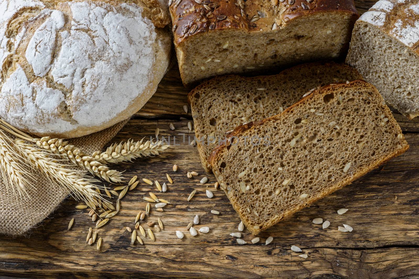 Group of dark breads with wheat, sunflower and rye grains on a wooden vintage table.