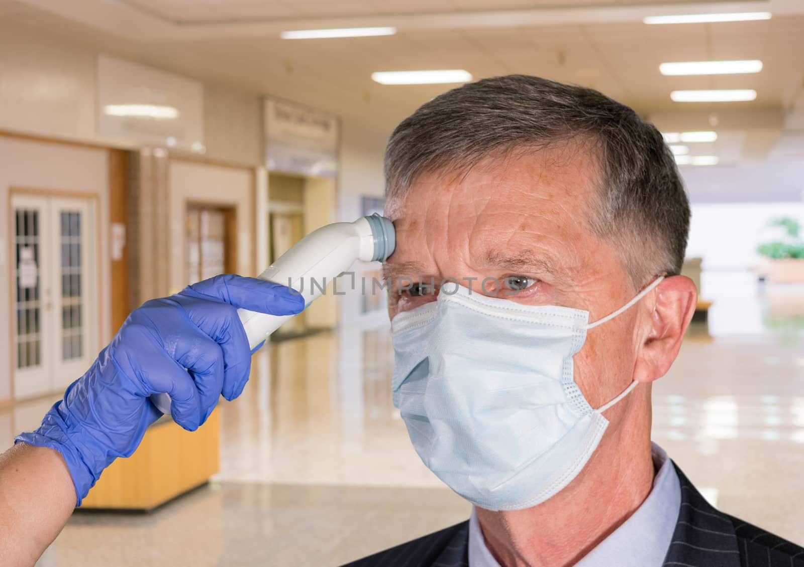 Mockup of hospital, clinic or shopping mall with senior adult wearing mask having a fever or temperature test taken to check coronavirus status