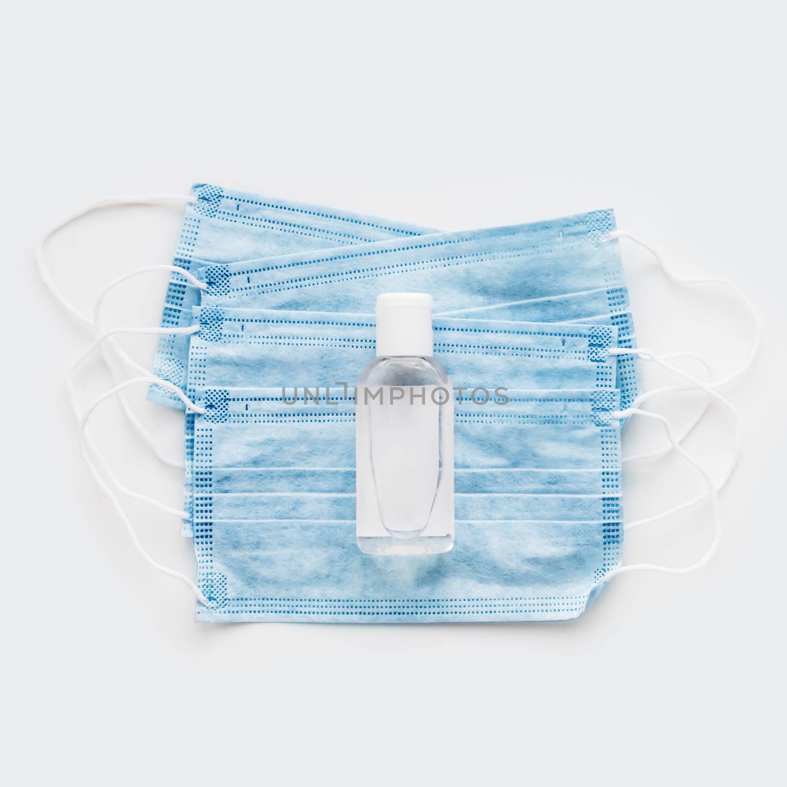 Top view on pack of blue protective medical masks with transparent bottle of sanitizer. Coronavirus COVID-19 concept on white background with copy space.