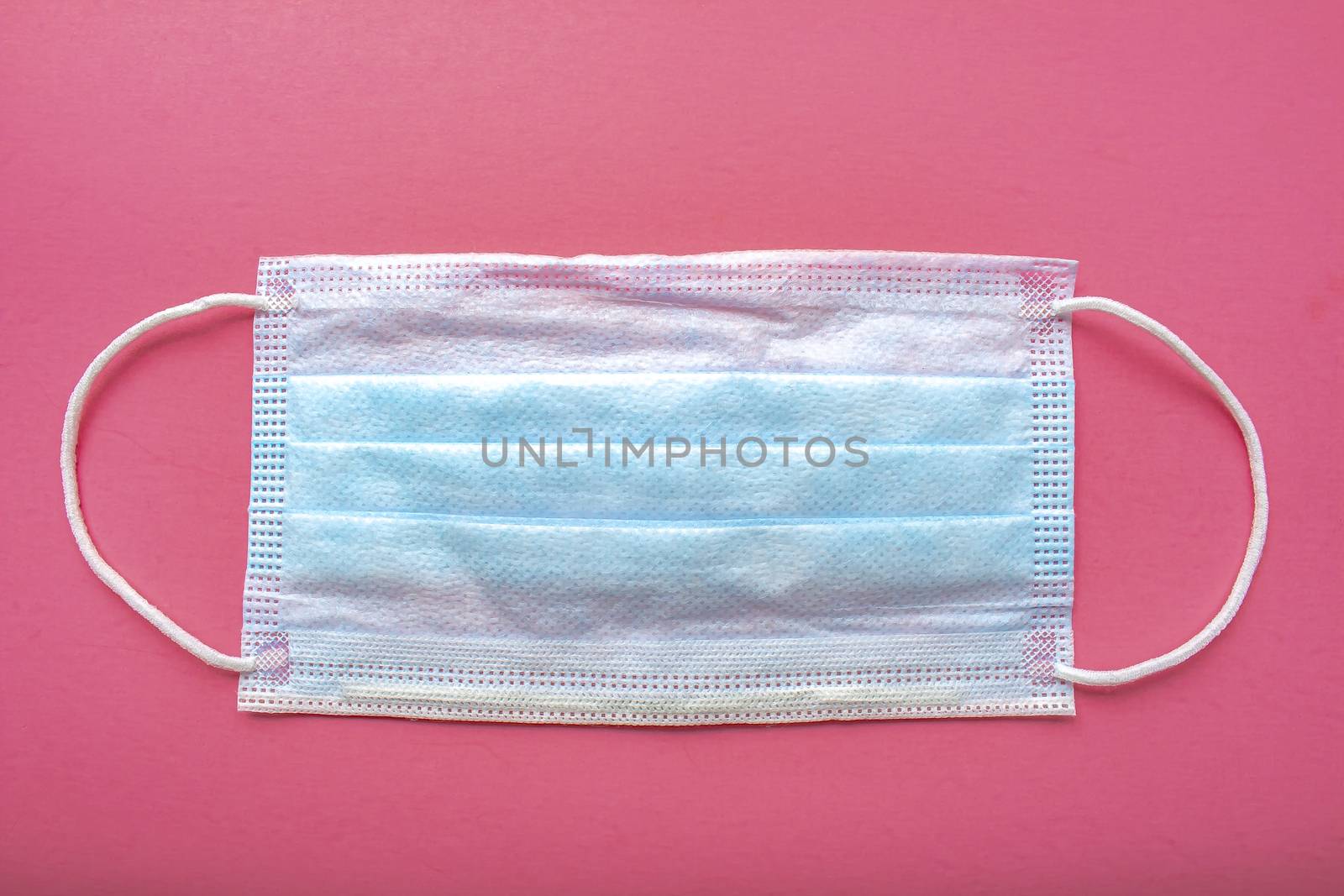 A medical surgical face mask on a pink background