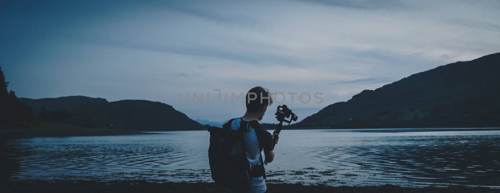 Person using a camera to film and shoot a lake in Scotland during sunset