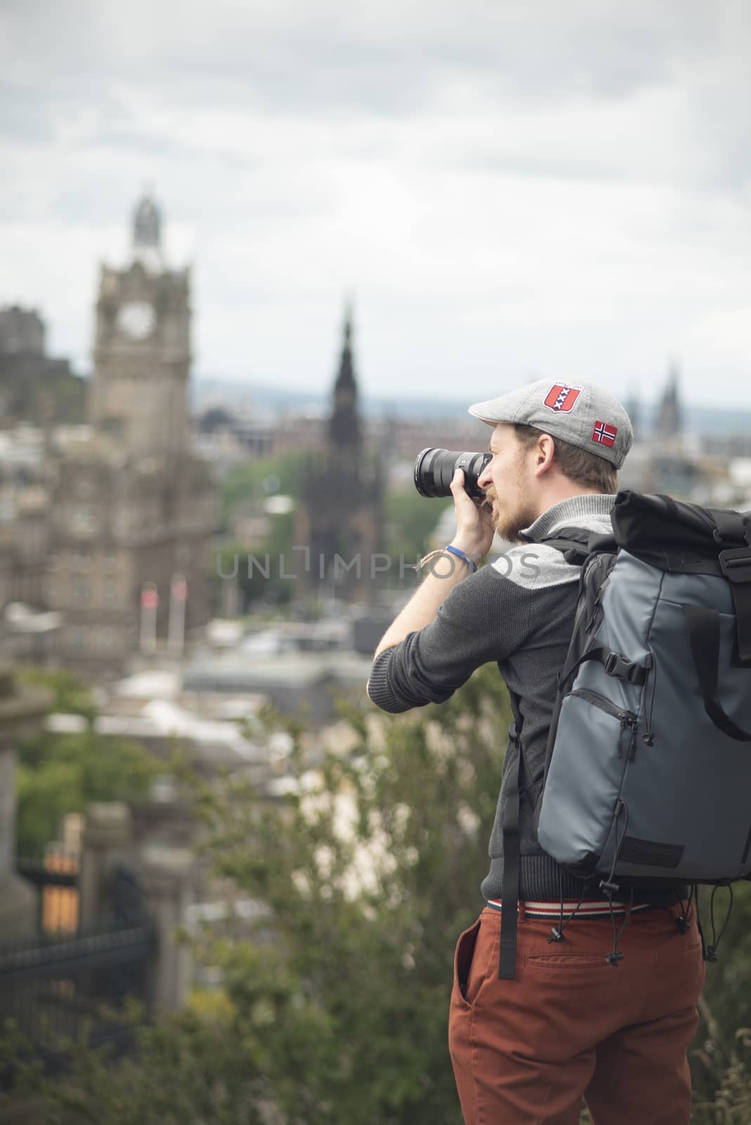 Photographer with backpack and a hat shooting buildings of Edinburgh in a sunny day