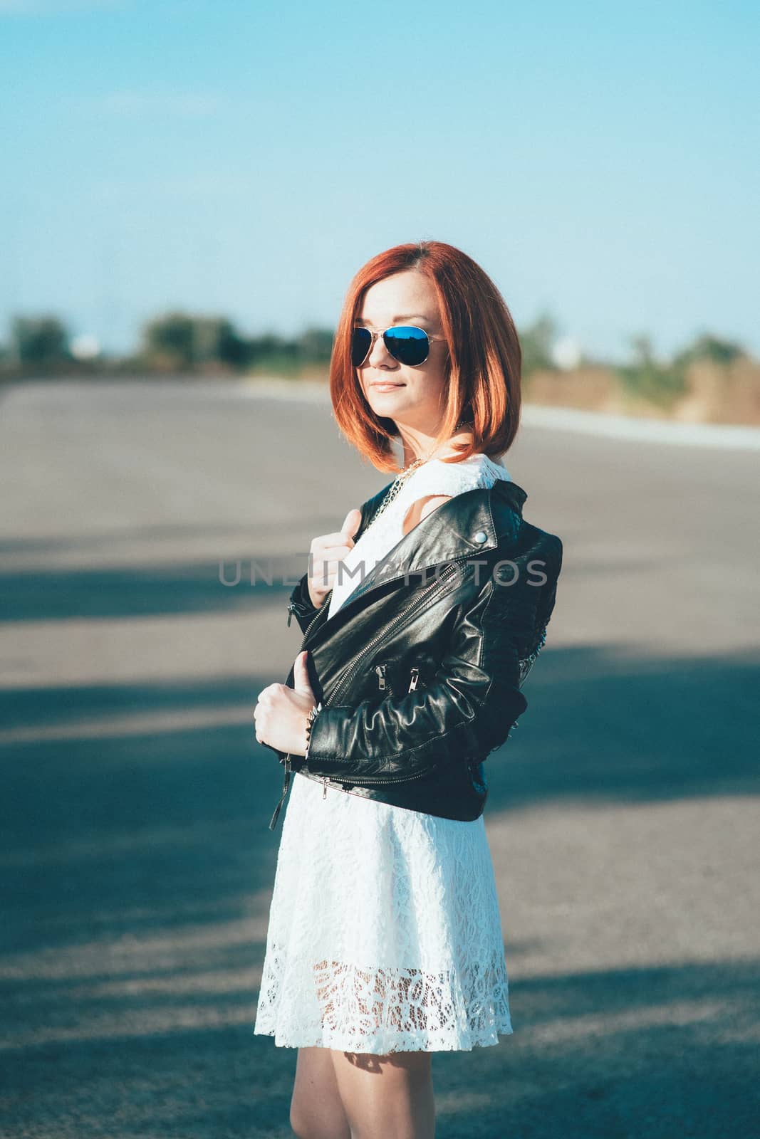 red-haired girl in a black jacket and blue glasses on a gray road