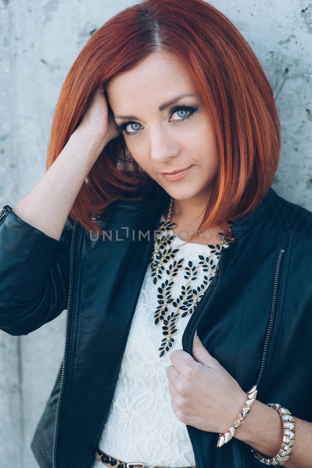 red-haired girl in a black jacket and blue glasses on a gray road