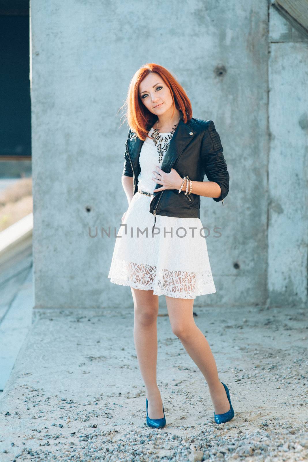 red-haired girl in a black jacket and blue glasses on a gray road