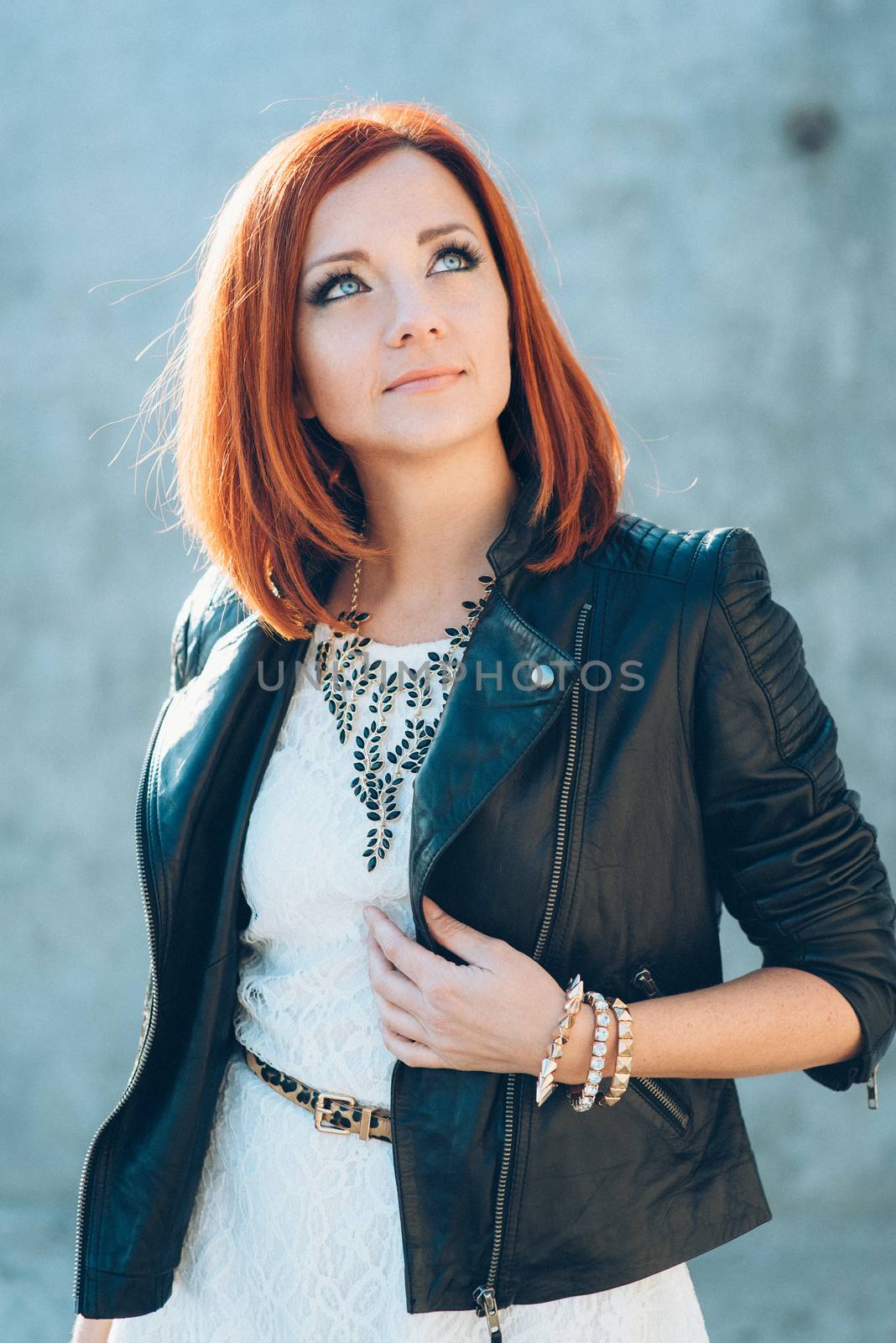 red-haired girl in a black jacket and blue glasses on a gray road