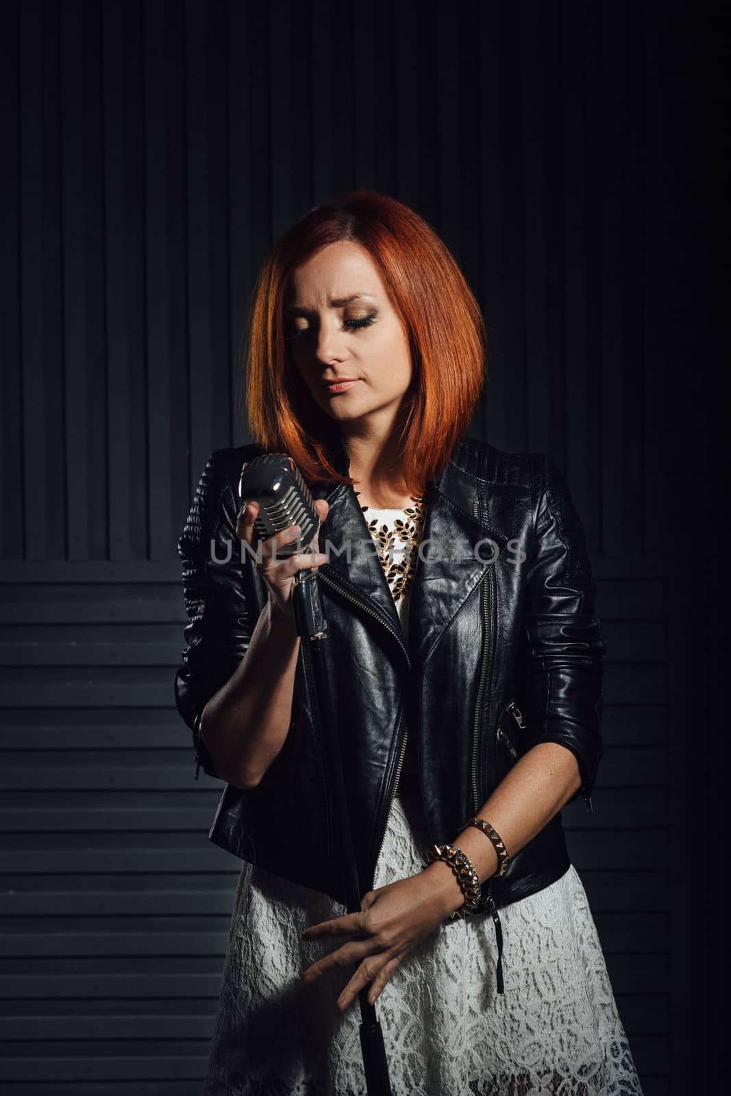 young red-haired girl in a white dress and a black leather rocker jacket sings emotionally into the microphone